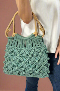 Model is holding a jade green colored cotton macrame bag with natural cain top handles. 