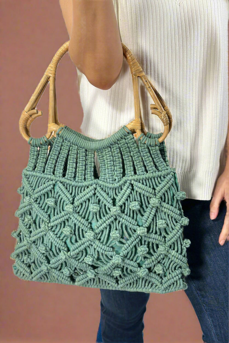 Model is holding a jade green colored cotton macrame bag with natural cain top handles. 