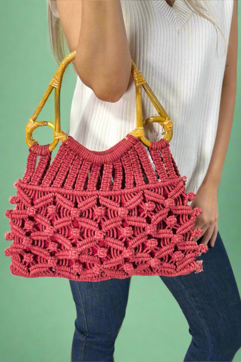 Model is holding a red colored cotton macrame woven bag with natural cain top handles. 