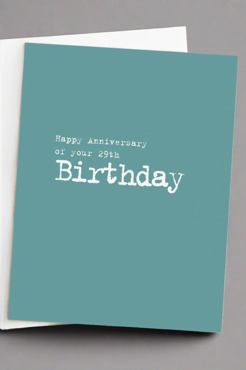 Minimalist greeting card in dusty teal with white lettering that reads ‘Happy Anniversary of your 29th Birthday’ and a white envelope.