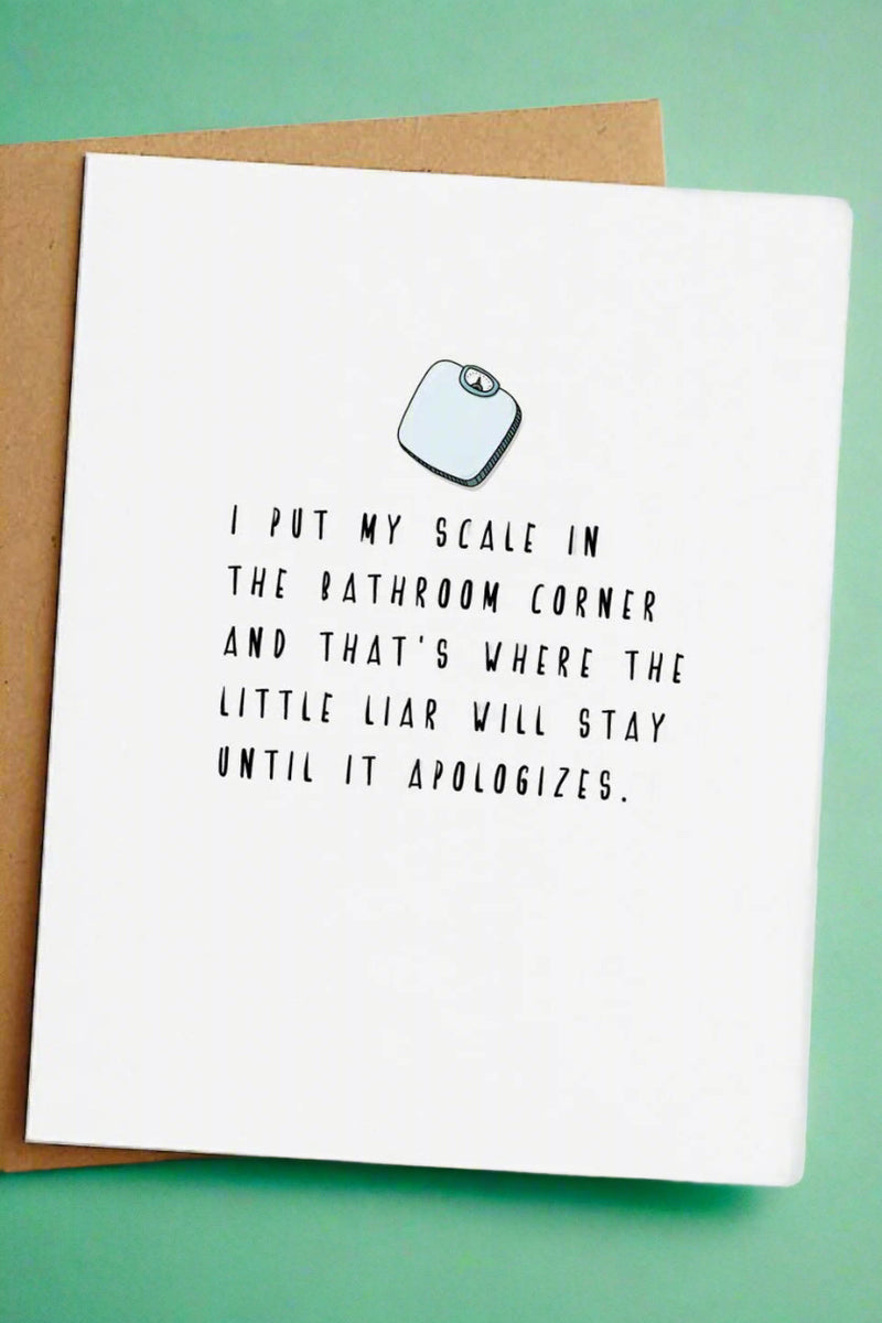 A white card with an image of a scale that says “I put my scale in the bathroom corner and that’s where the little liar will stay until it apologizes.“