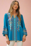 A teal blouse with geometric embroidery and bell sleeves.