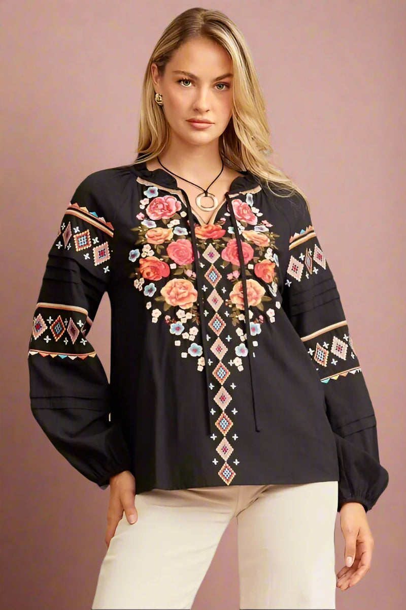 A black long sleeve floral embroidered blouse. This light weight blouse has a tie neck and cinched sleeves.