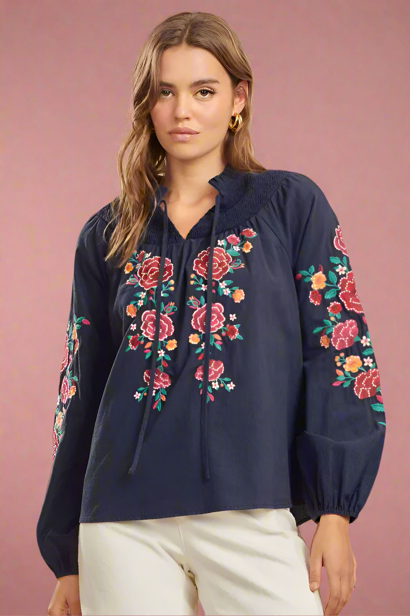 A dark blue, smocked tie neckline blouse with floral embroidery.