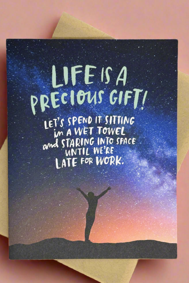 Card with image of person with arms raised to nighttime starry sky and words “Life is a precious gift! Let’s spend it sitting in a wet towel, and staring into space until we’re late for work.“