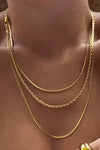 Gold layered necklace with three tiers. The first is a thin round chain, the second is braided, and third is a flat herringbone chain.