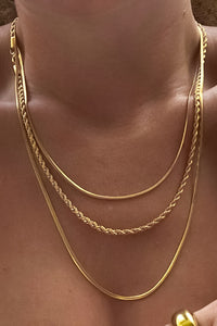 Gold layered necklace with three tiers. The first is a thin round chain, the second is braided, and third is a flat herringbone chain.