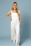 Model is wearing a white lace wide leg jumpsuit that is fully lined and features a square neckline and zipper in back for entry.