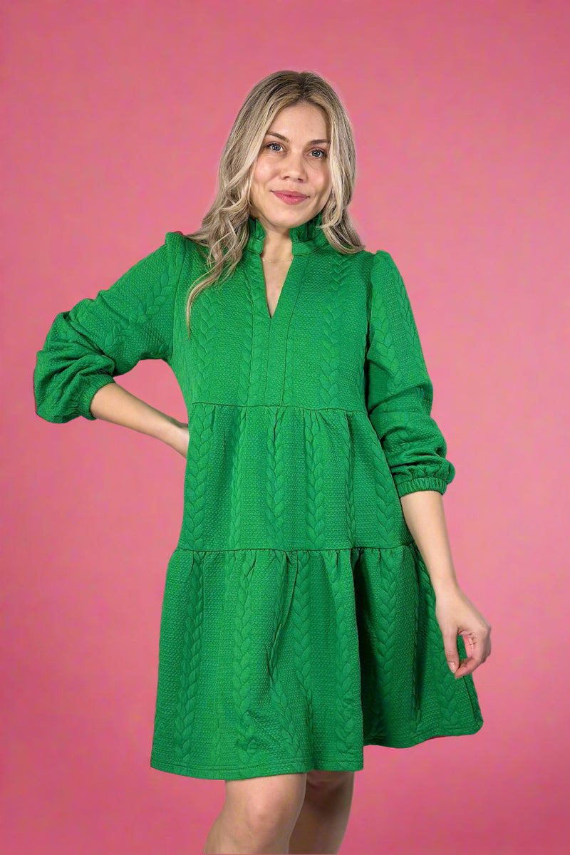 Model is wearing a kelly green colored long sleeve tiered mini dress with a ruffled collar detail and unique cable knit texture. 