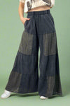 Model is wearing long charcoal grey tiered wide leg pants that feature eyelet detailing.