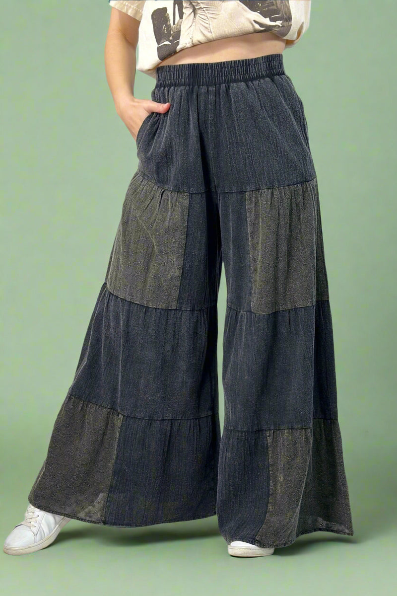 Model is wearing long charcoal grey tiered wide leg pants that feature eyelet detailing.