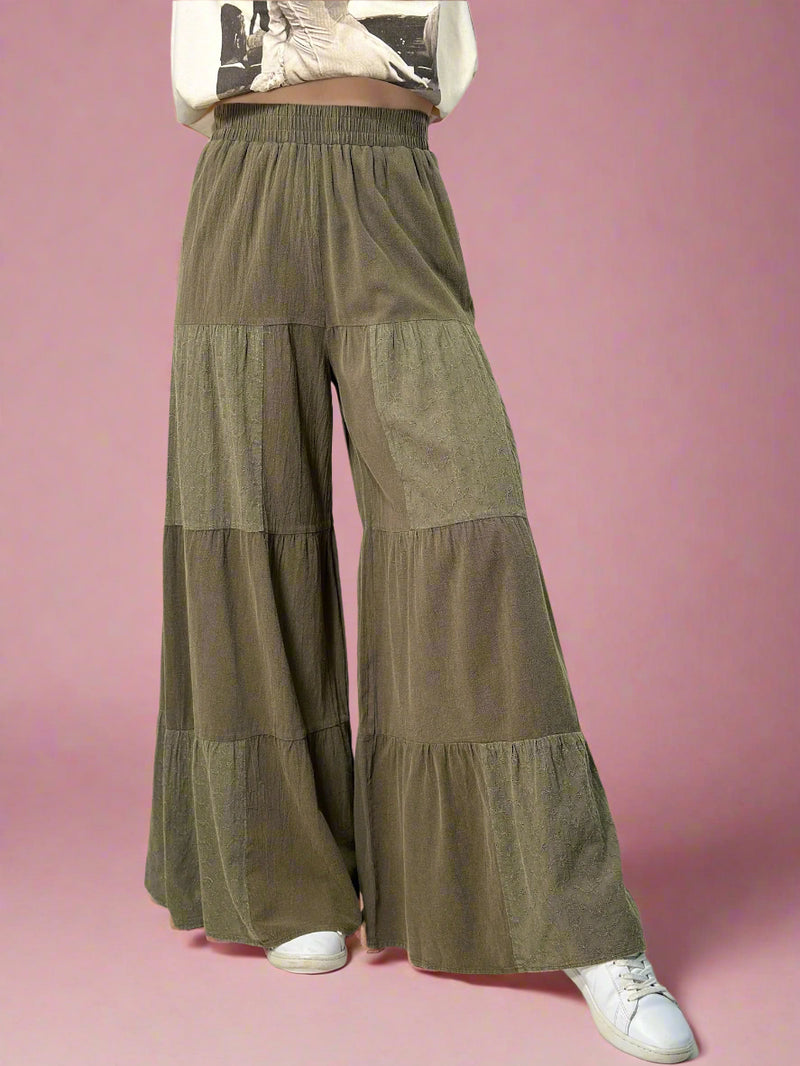 Model is wearing olive colored tiered pants with an elastic waist and eyelet patchwork detailing. 