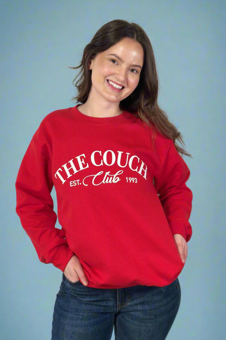 Model is wearing a red colored fleece lined crew neck with the phrase "The Couch Club" printed across the front in velvet lettering. 