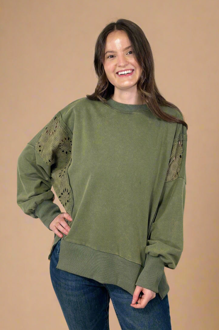 Model is wearing an olive green colored crew neck top featuring eyelet patchwork detailing.