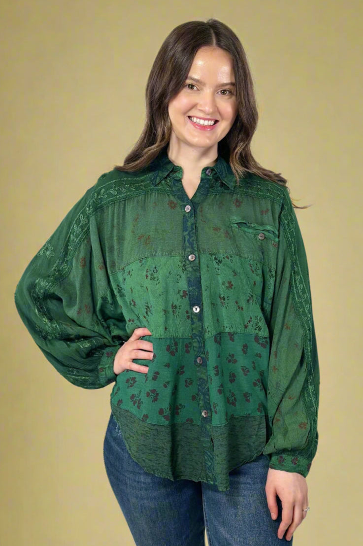 Model is wearing an oversized flowy button up blouse in a beautiful deep green color with pattern detailing. 