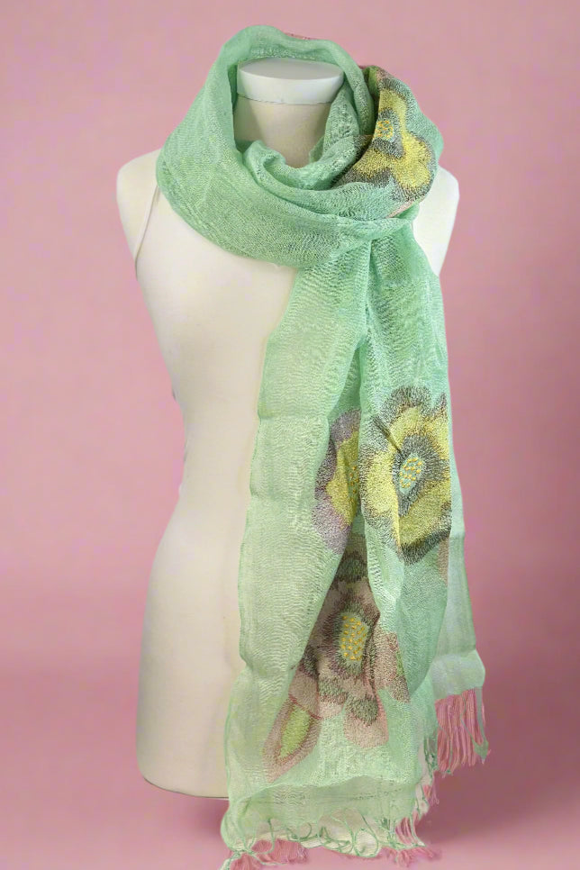 Sheer light green linen scarf featuring fringe and embroidered flowers. 