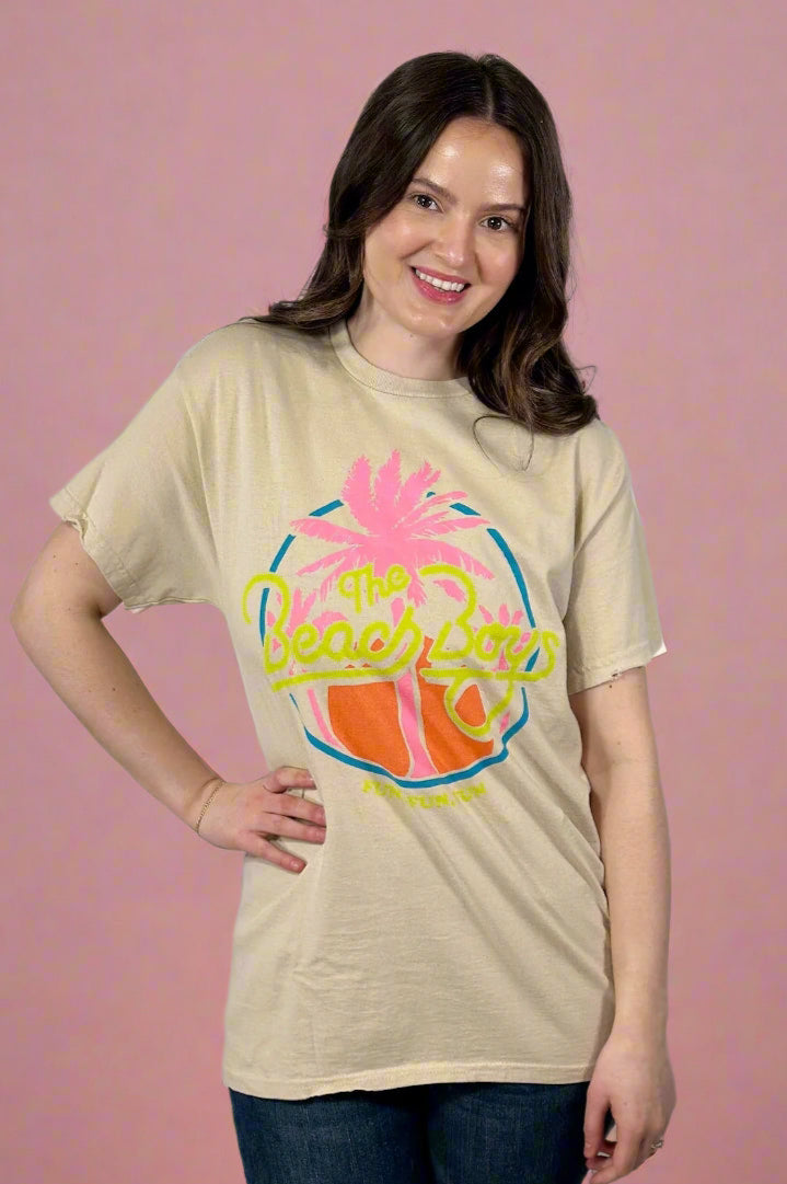 Model is wearing a tan colored vintage style tee shirt with a neon colored retro Beach Boys logo.