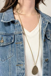 Model is wearing a long teardrop pendant necklace in gold