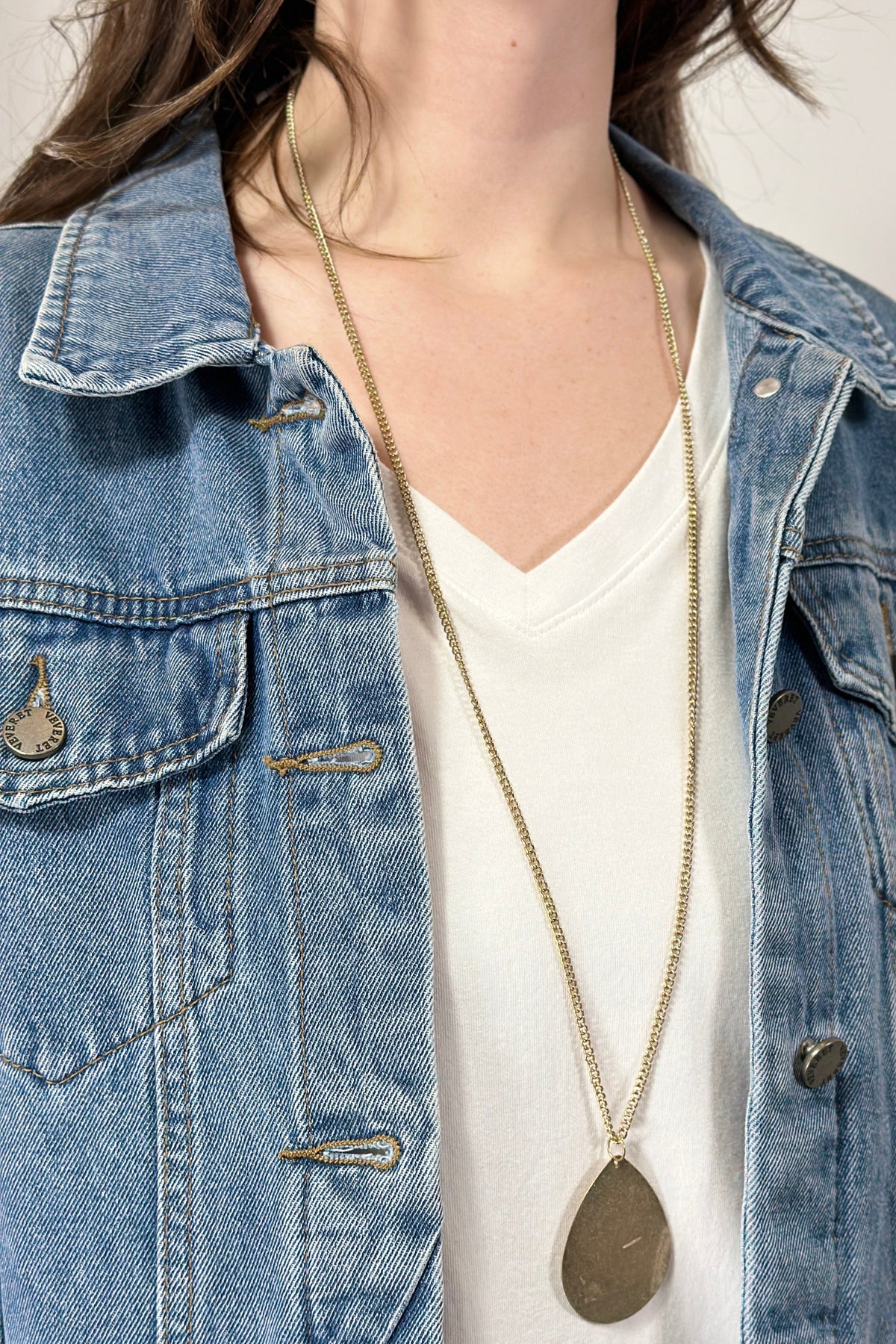 Model is wearing a long teardrop pendant necklace in gold