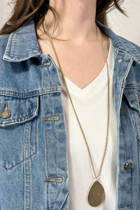Model is wearing a long teardrop pendant necklace in gold