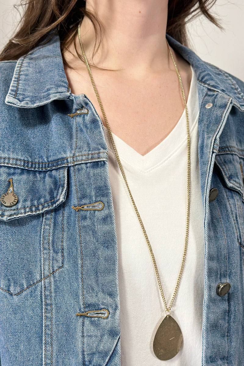 Model is wearing a long teardrop pendant necklace in gold