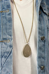 Model is wearing a long teardrop pendant necklace in gold