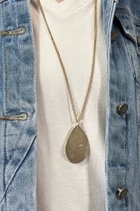 Model is wearing a long teardrop pendant necklace in gold