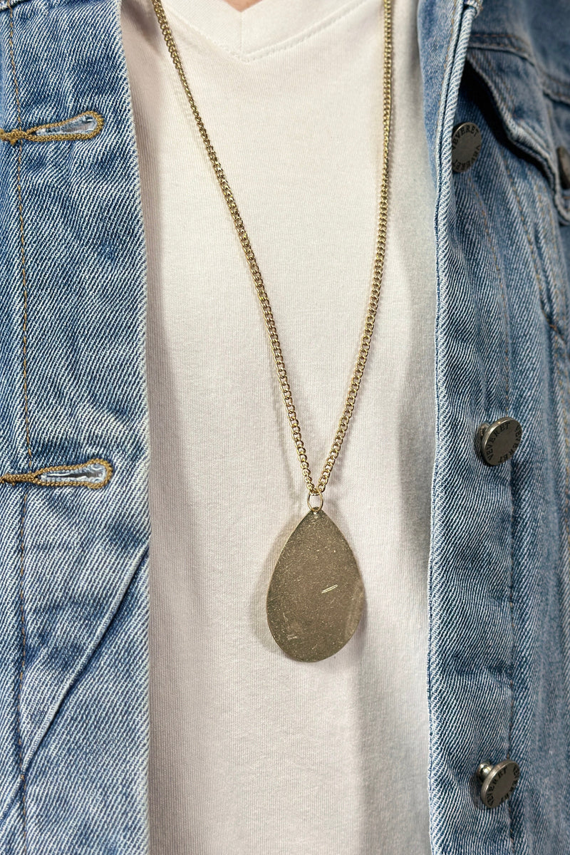 Model is wearing a long teardrop pendant necklace in gold