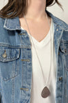 Model is wearing a long teardrop pendant necklace in silver