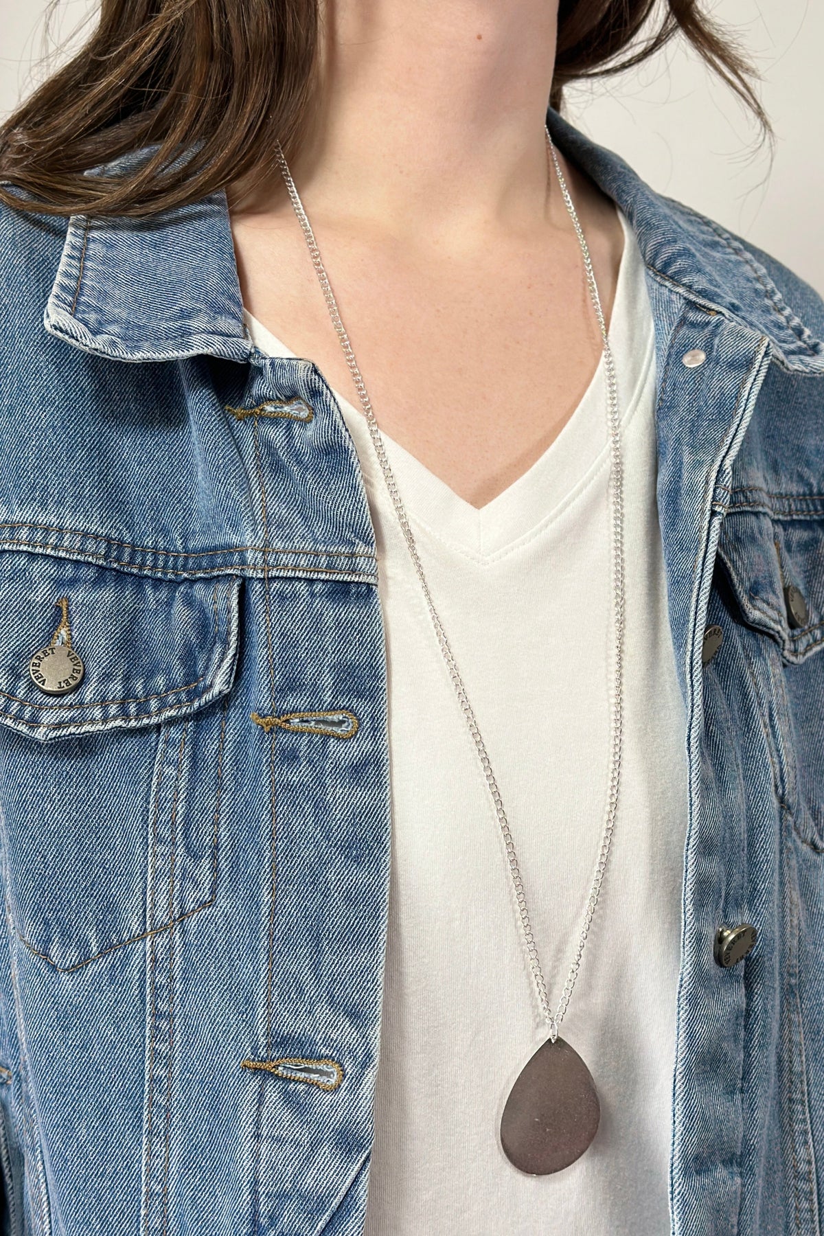 Model is wearing a long teardrop pendant necklace in silver