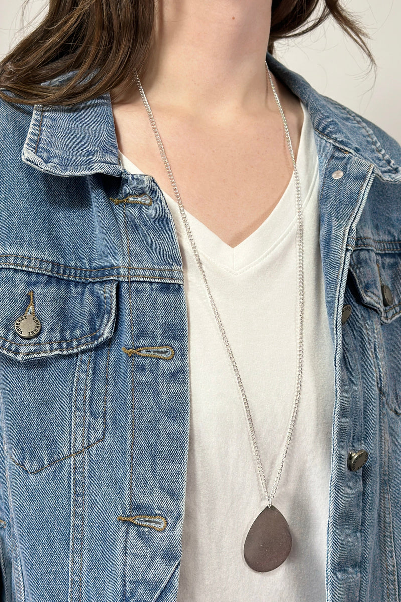 Model is wearing a long teardrop pendant necklace in silver