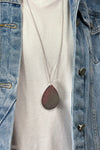 Model is wearing a long teardrop pendant necklace in silver