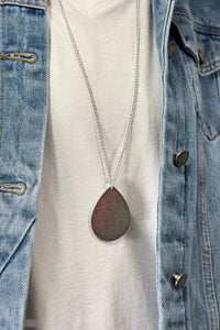 Model is wearing a long teardrop pendant necklace in silver
