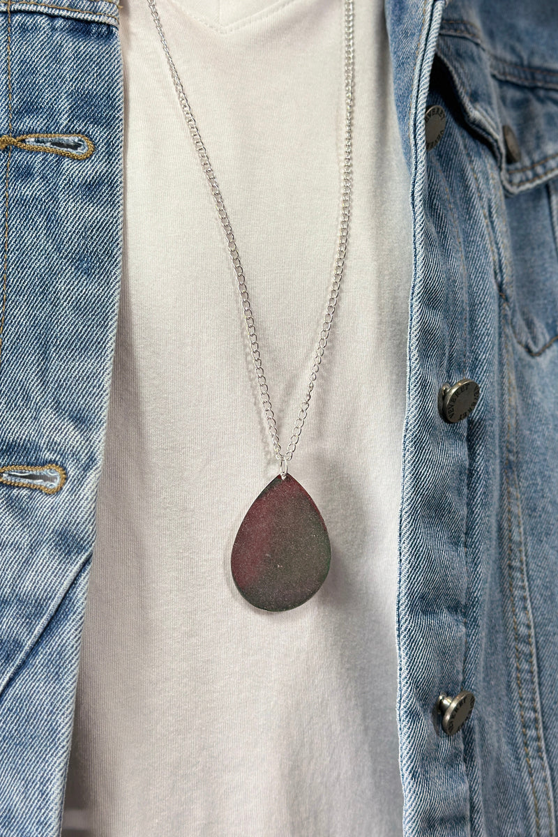 Model is wearing a long teardrop pendant necklace in silver