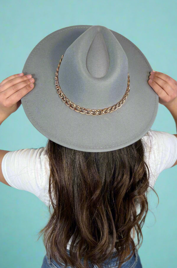 Model showcases light grey, wide brim, fedora hat with gold chain accent trim.