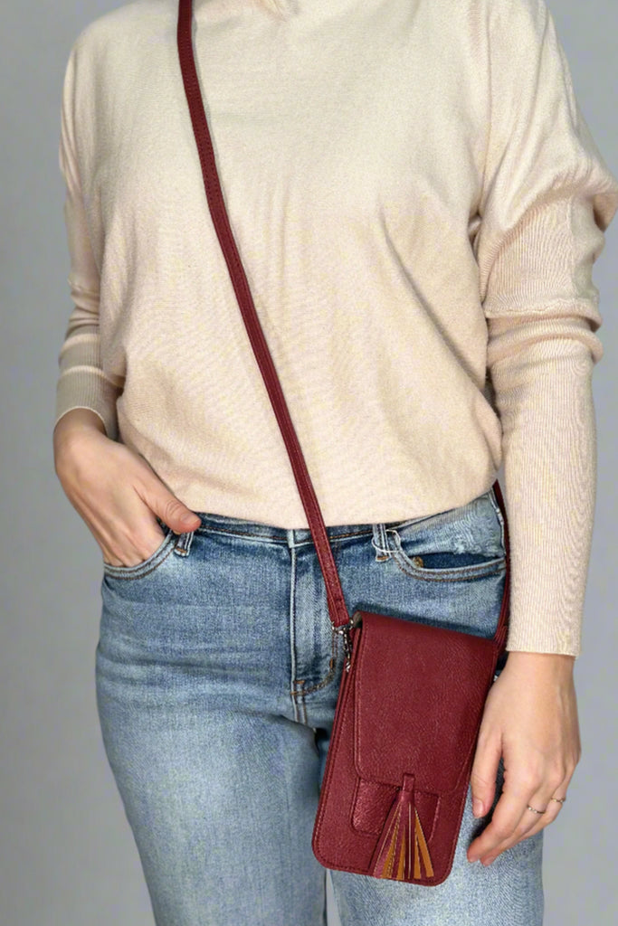 A red, small cross body bag. It has a close flap and tassel detail.