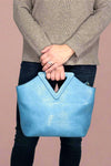 Women’s handbag in light blue with triangular handle and removable adjustable crossbody strap.