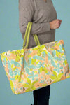 Large canvas tote with bright floral print in green, teal, and peach with metallic accent.
