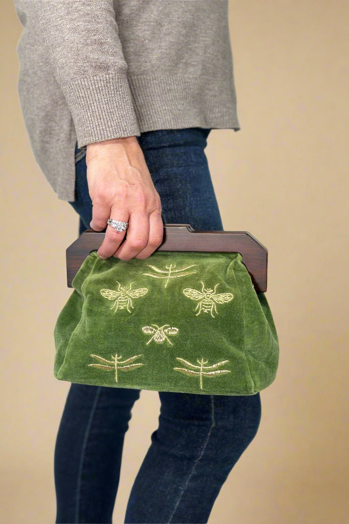 Green velvet clutch bag with wooden handle and embroidered bee and dragonfly detail.