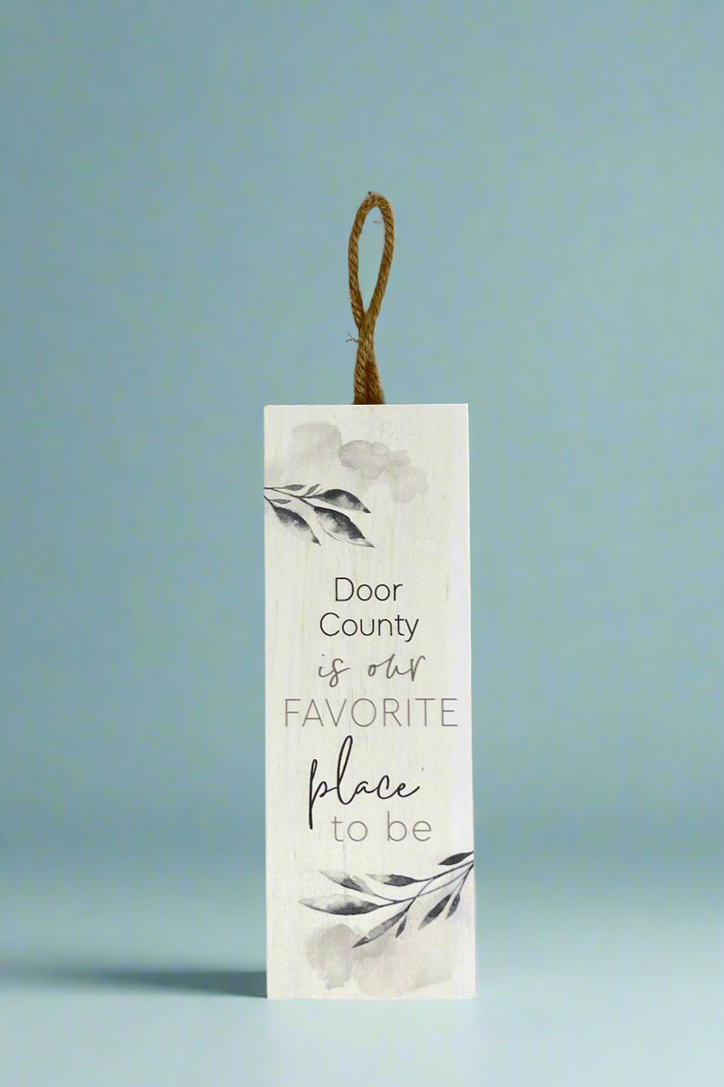 A vertical sign with rope hanging that says “Door County is our favorite place to be.”