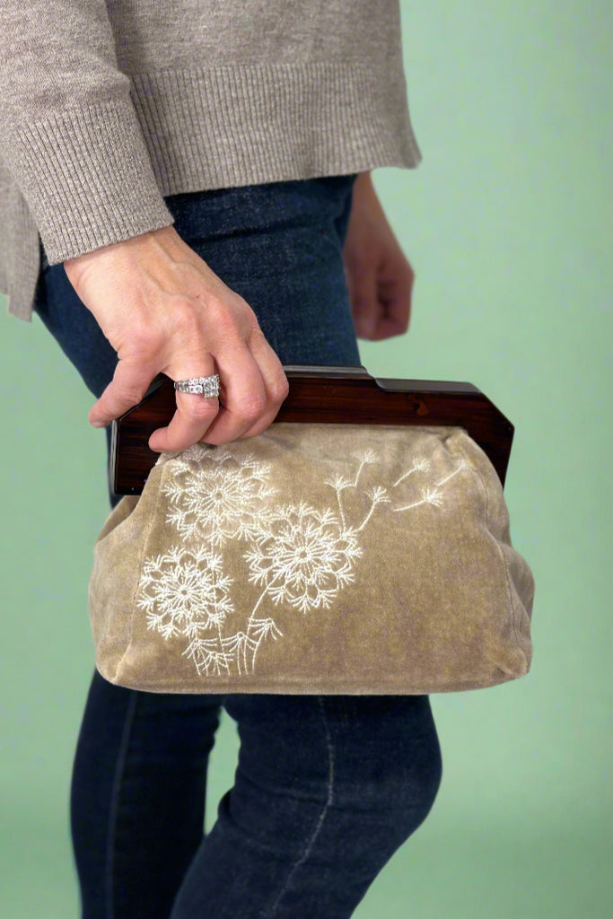 Beige velvet clutch with wooden handle and white embroidered dandelion detail.