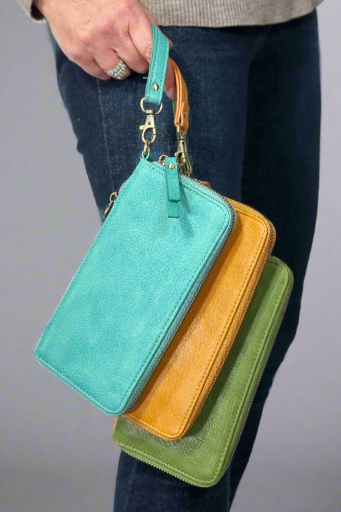 Model is holding 3 wallets with zipper closure and wristlet straps in teal, mustard yellow, and olive green.