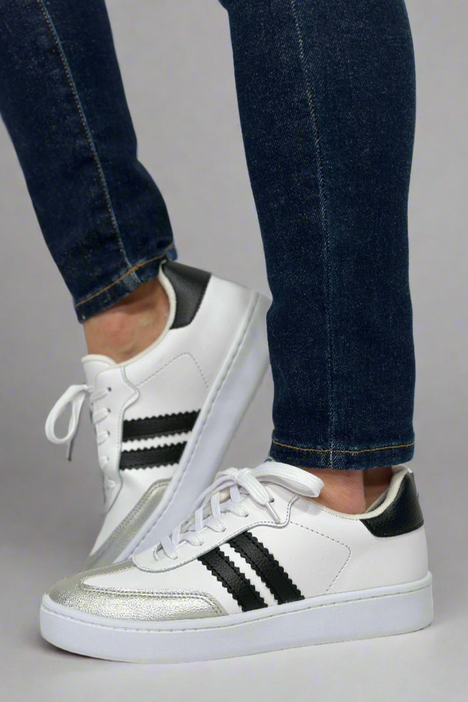 Model is wearing black and white soccer style sneakers with two black stripes. 