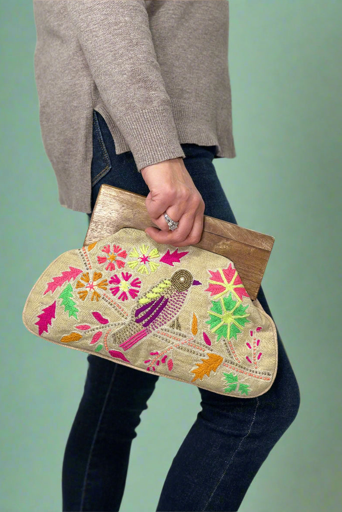 Model is holding a wooden handle clutch with embroidered detailing. 