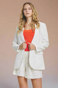 Model is wearing a crisp white lace blazer with small shoulder pads and a single button in the front. 