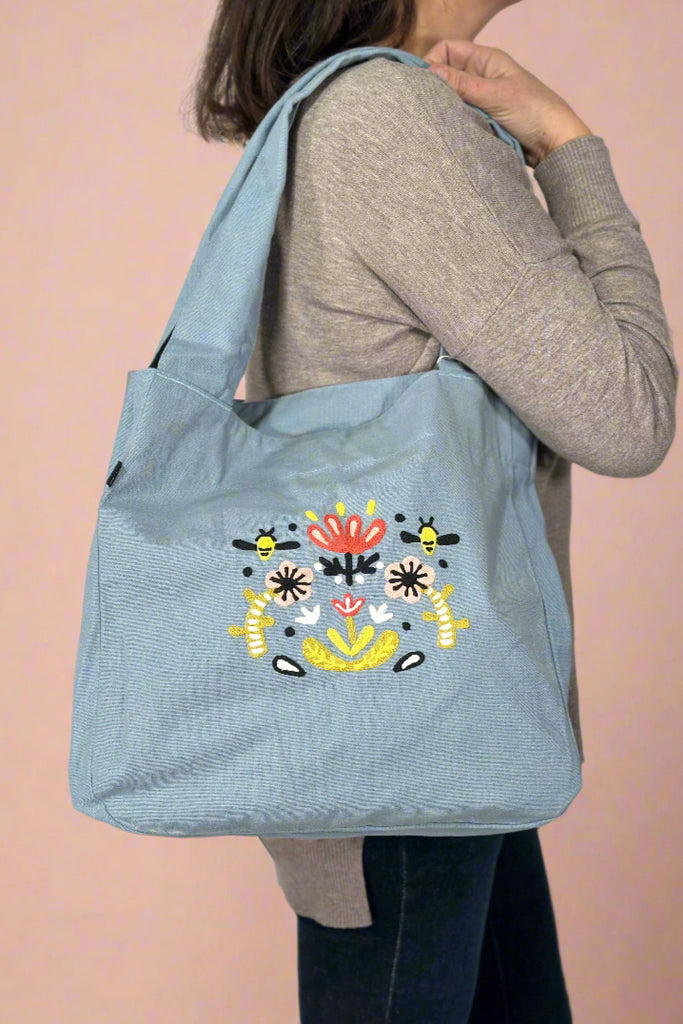 Model is wearing an embroidered tote bag. 