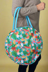 Model is holding a fruit printed round cooler bag with top handles. 