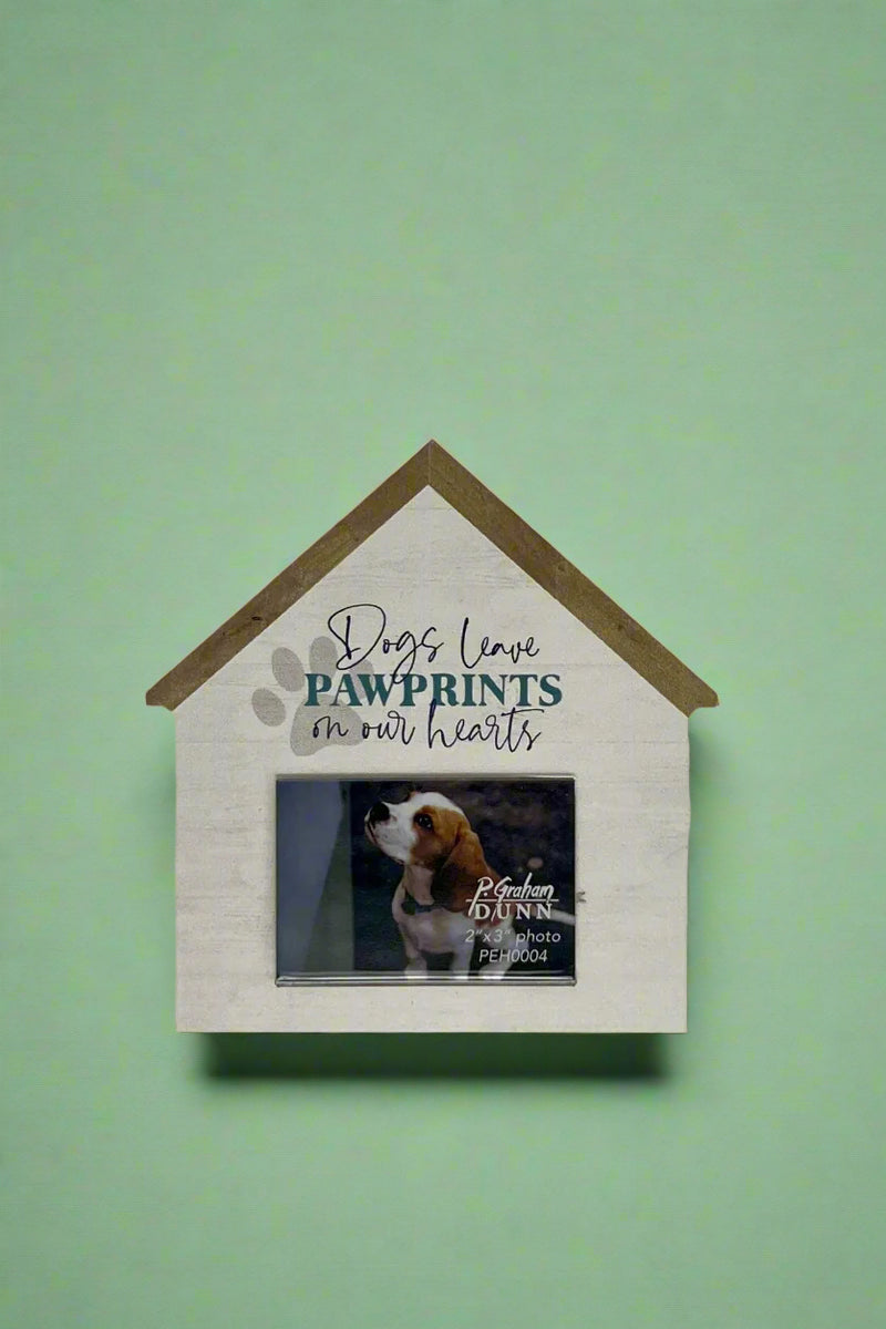 A wooden picture frame in the shape of a house with a dog paw print and lettering that reads “Dogs leave paw prints on our hearts.”