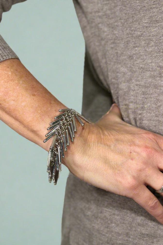 Model is wearing a silver bracelet that features metal fringe. 