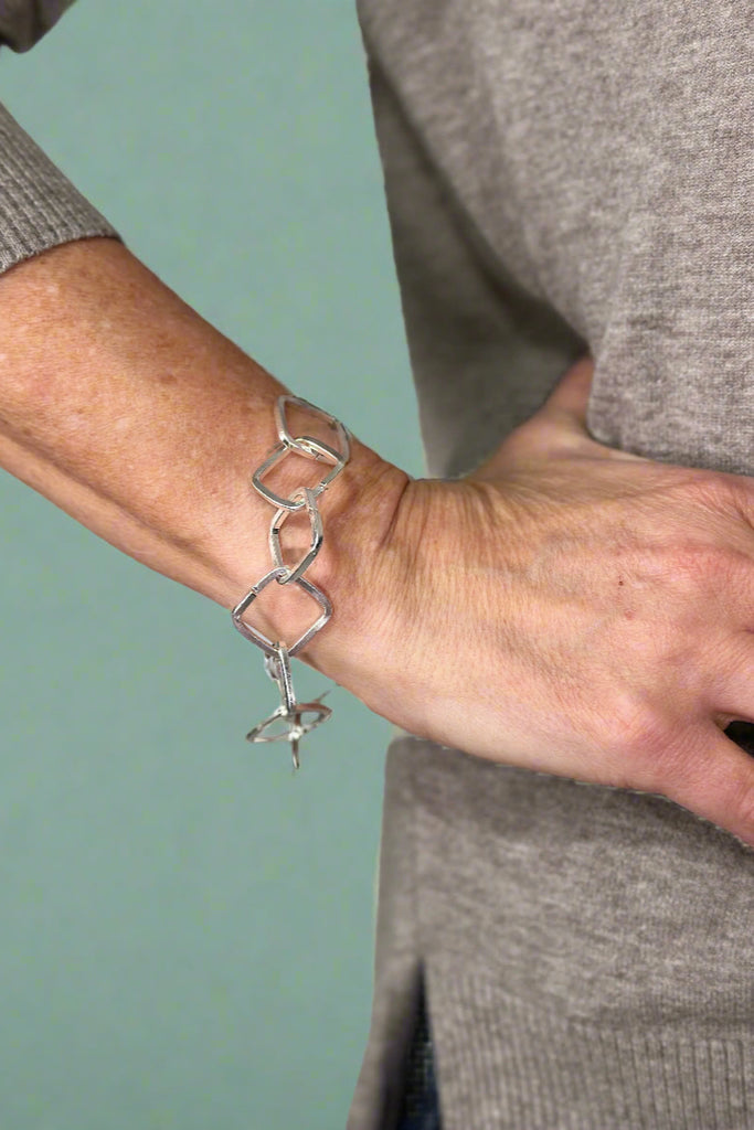 Model is wearing a silver square chain bracelet. 